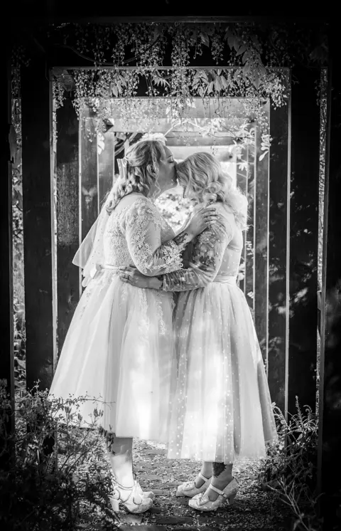 The newlywed brides enjoy a kiss amongst the leaves