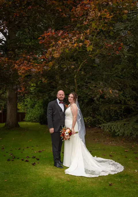 The bride and groom pose amongst the autumn colours, matching the bouquet