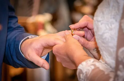 The bride places the wedding ring on the groom's finger in their church wedding service